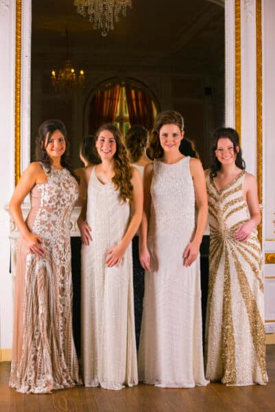 a group of young ladies in gold dresses by a fireplace